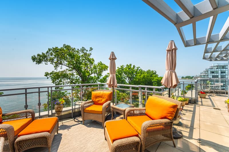 The terrace of the suite on Lakeshore Road: wicker chairs with orange cushions under a white pergola, mature oaks and Lake Ontario beyond